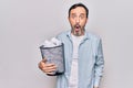 Middle age handsome man holding full paper bin of crumpled papers over white background scared and amazed with open mouth for Royalty Free Stock Photo