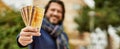 Middle age handsome man holding norwegian krone banknotes outdoors at the park