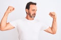 Middle age handsome man wearing casual t-shirt standing over isolated white background showing arms muscles smiling proud