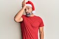 Middle age handsome man wearing christmas hat and summer t-shirt surprised with hand on head for mistake, remember error