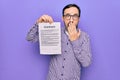 Middle age handsome man wearing glasses holding contract document over purple background covering mouth with hand, shocked and Royalty Free Stock Photo