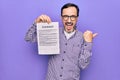Middle age handsome man wearing glasses holding contract document over purple background pointing thumb up to the side smiling Royalty Free Stock Photo