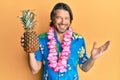 Middle age handsome man wearing hawaiian lei holding pineapple celebrating achievement with happy smile and winner expression with Royalty Free Stock Photo