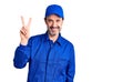 Middle age handsome man wearing mechanic uniform smiling looking to the camera showing fingers doing victory sign Royalty Free Stock Photo