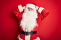 Middle age handsome man wearing Santa costume standing over isolated red background relaxing and stretching, arms and hands behind