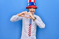 Middle age handsome patriotic man wearing united states hat and tie over blue background smiling in love doing heart symbol shape