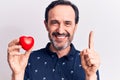 Middle age handsome romantic man holding plastic heart over isolated white background smiling with an idea or question pointing Royalty Free Stock Photo
