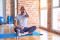 Middle age handsome sportman sitting on mat doing stretching yoga exercise at gym surprised with hand on head for mistake,