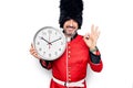 Middle age handsome wales guard man wearing traditional uniform holding big clock doing ok sign with fingers, smiling friendly