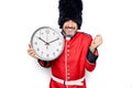 Middle age handsome wales guard man wearing traditional uniform holding big clock screaming proud, celebrating victory and success