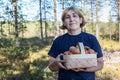 Middle age happy woman holding basketful of mushrooms with orange caps, stands in forest