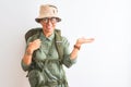 Middle age hiker woman wearing backpack canteen hat glasses over isolated white background smiling cheerful presenting and Royalty Free Stock Photo