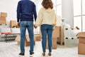 Middle age hispanic couple on back view holding hands and standing at new home