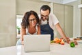 Middle age hispanic couple cooking and using laptop at kitchen Royalty Free Stock Photo