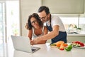 Middle age hispanic couple cooking and using laptop at kitchen Royalty Free Stock Photo