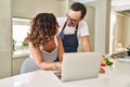 Middle age hispanic couple cooking and using laptop at kitchen Royalty Free Stock Photo