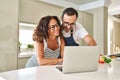 Middle age hispanic couple cooking and using laptop at kitchen Royalty Free Stock Photo