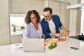 Middle age hispanic couple cooking and using laptop at kitchen Royalty Free Stock Photo