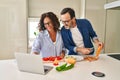 Middle age hispanic couple cooking and using laptop at kitchen Royalty Free Stock Photo