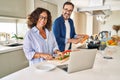 Middle age hispanic couple cooking and using laptop at kitchen Royalty Free Stock Photo