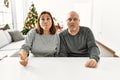 Middle age hispanic couple sitting on the table by christmas tree making fish face with lips, crazy and comical gesture Royalty Free Stock Photo