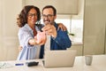 Middle age hispanic couple smiling confident saving coin on piggy bank at kitchen Royalty Free Stock Photo