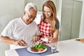 Middle age hispanic couple smiling happy eating beef with salad at the kitchen Royalty Free Stock Photo