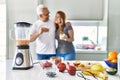 Middle age hispanic couple smiling happy and hugging drinking glass of smoothie at the kitchen