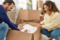 Middle age hispanic couple smiling happy playing with dog and foam package at new home