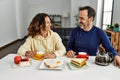 Middle age hispanic couple smiling happy sitting on the table having breakfast at home Royalty Free Stock Photo