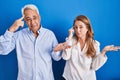 Middle age hispanic couple standing over blue background confused and annoyed with open palm showing copy space and pointing Royalty Free Stock Photo