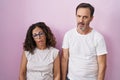 Middle age hispanic couple together over pink background looking sleepy and tired, exhausted for fatigue and hangover, lazy eyes