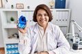 Middle age hispanic dentist woman working at dentist clinic holding invisible aligner looking positive and happy standing and