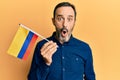 Middle age hispanic man holding colombia flag scared and amazed with open mouth for surprise, disbelief face Royalty Free Stock Photo