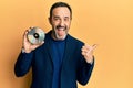 Middle age hispanic man holding compact disc pointing thumb up to the side smiling happy with open mouth