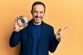 Middle age hispanic man holding compact disc smiling happy pointing with hand and finger to the side Royalty Free Stock Photo