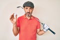 Middle age hispanic man holding golf club and ball relaxed with serious expression on face
