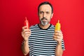 Middle age hispanic man holding ketchup and mustard bottle puffing cheeks with funny face