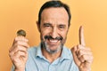 Middle age hispanic man holding virtual currency ethereum coin smiling with an idea or question pointing finger with happy face,