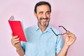 Middle age hispanic man reading book holding glasses smiling looking to the side and staring away thinking Royalty Free Stock Photo