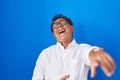 Middle age hispanic man standing over blue background laughing at you, pointing finger to the camera with hand over body, shame Royalty Free Stock Photo