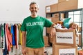 Middle age hispanic man wearing volunteer t shirt at donations stand with a happy and cool smile on face