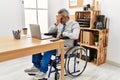 Middle age hispanic man working at the office sitting on wheelchair with sad expression covering face with hands while crying Royalty Free Stock Photo