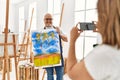 Middle age hispanic painter couple smiling happy making photo using smartphone at art studio