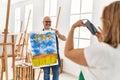 Middle age hispanic painter couple smiling happy making photo using smartphone at art studio