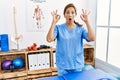 Middle age hispanic physiotherapist woman working at pain recovery clinic looking surprised and shocked doing ok approval symbol Royalty Free Stock Photo