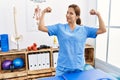Middle age hispanic physiotherapist woman working at pain recovery clinic showing arms muscles smiling proud Royalty Free Stock Photo