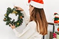 Middle age hispanic woman on back view hanging christmas decor on door at home