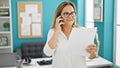 Middle age hispanic woman business worker speaking on the phone reading document at the office Royalty Free Stock Photo