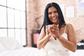 Middle age hispanic woman drinking cup of coffee sitting on bed at bedroom Royalty Free Stock Photo